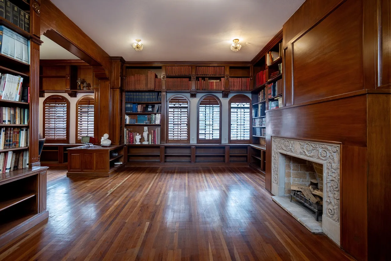 Biblioteca con ventanales, libreros de madera y chimenea de cantera