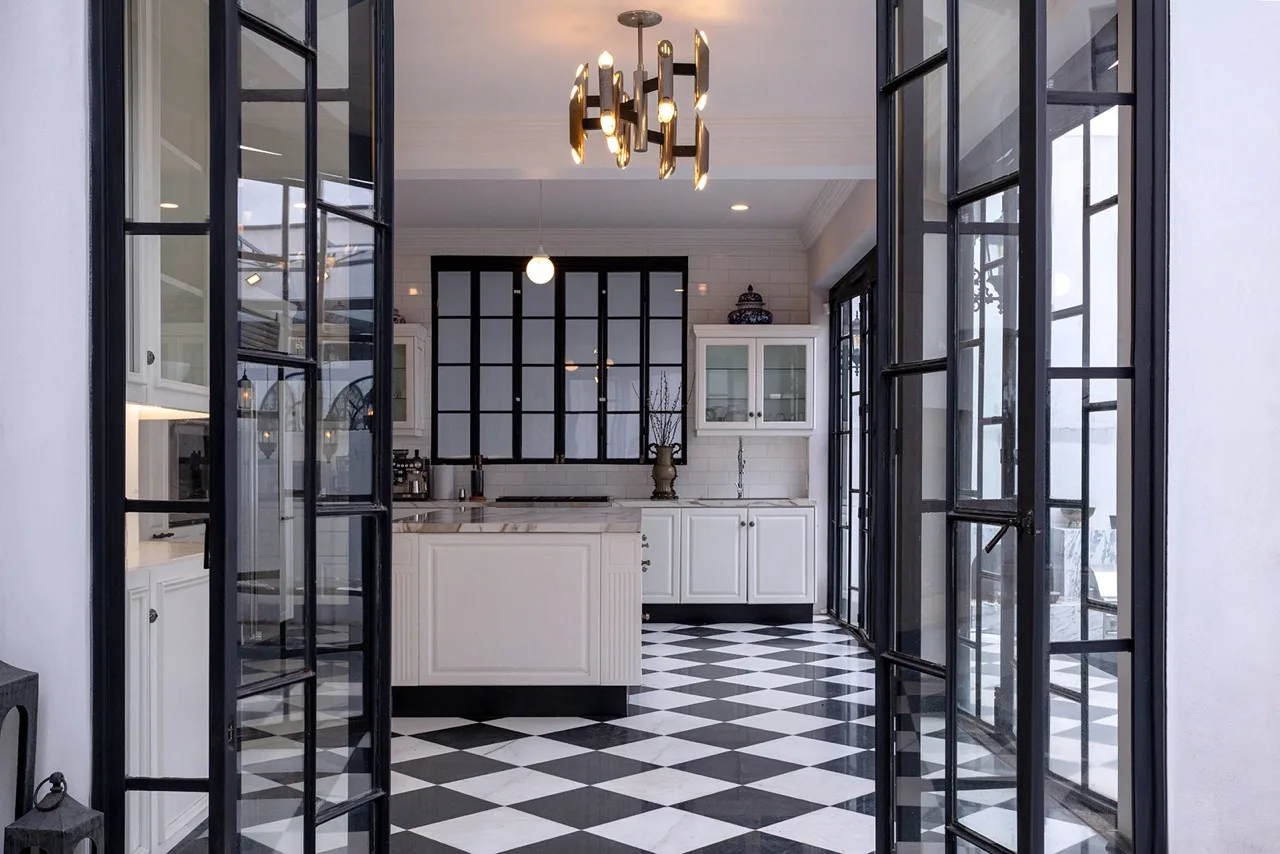 Cocina con piso en damero blanco y negro, cancelería de herrería y candil de latón