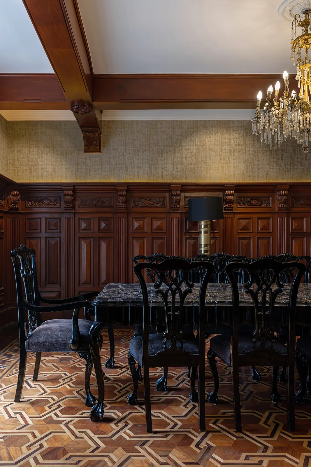 Comedor con boiserie de madera labrada, candil dorado y piso de marquetería geométrica