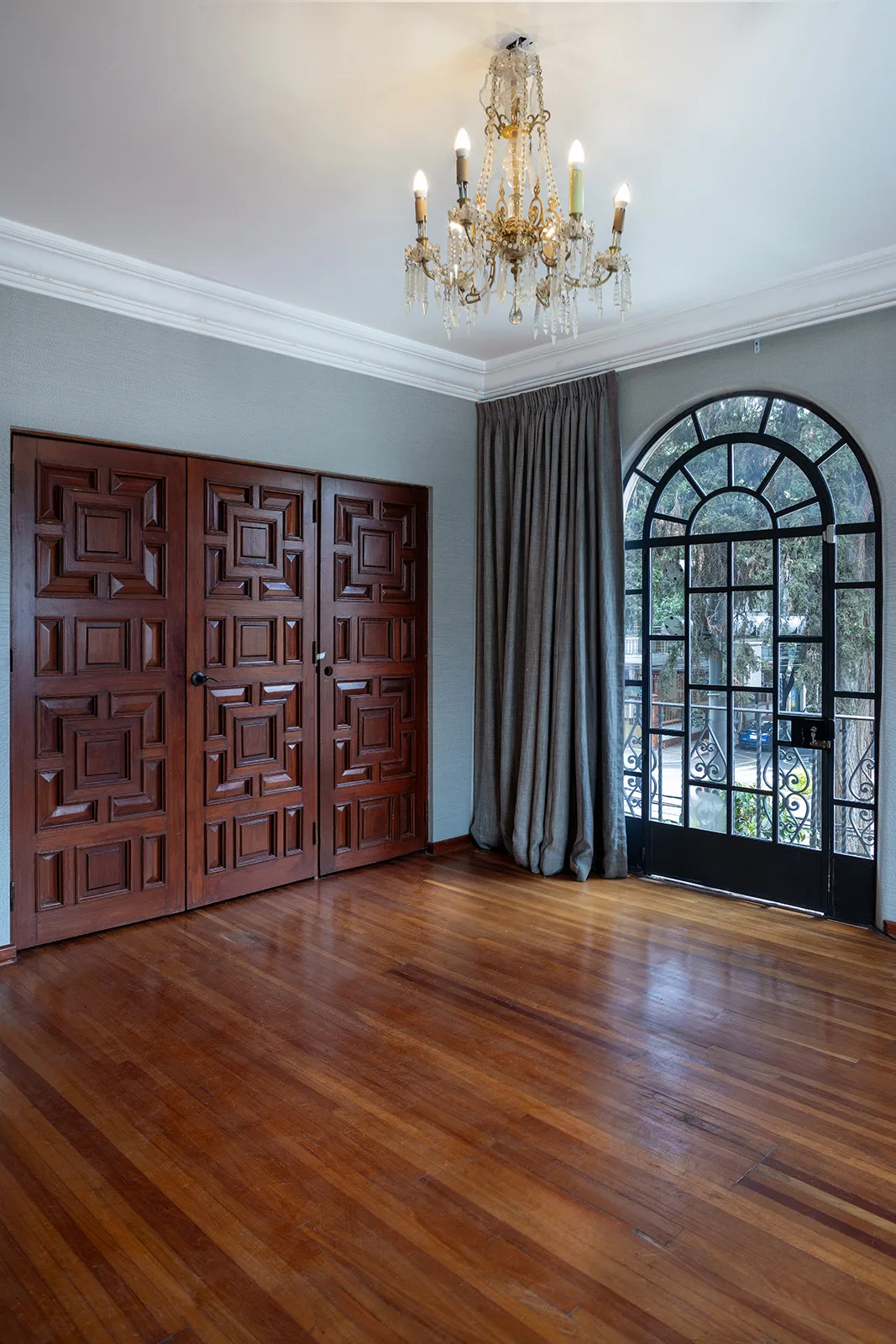 Sala con puerta de madera labrada, candil de cristal y ventanal arqueado de herrería
