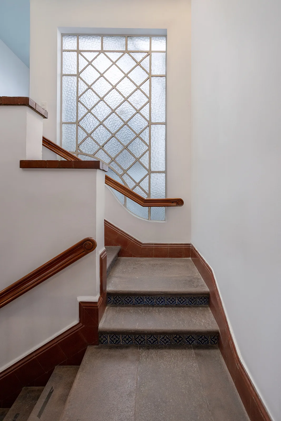 Escalera de servicio con pasamanos de madera y ventanal de vitroblock